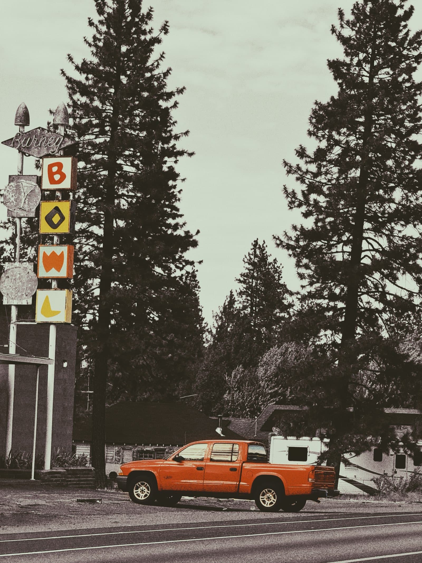 Retro bowling alley sign with orange truck and pine trees