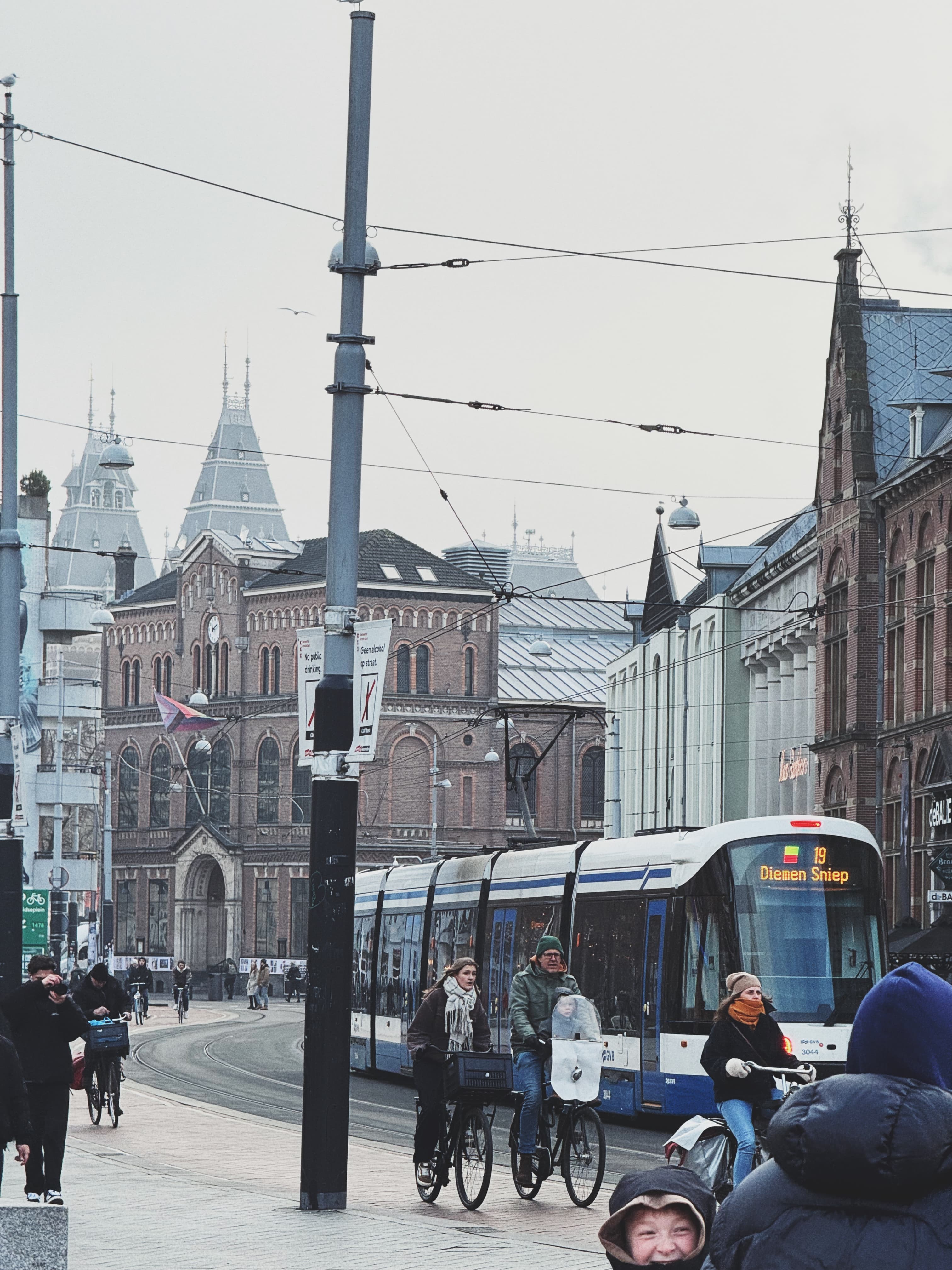 Amsterdam tram passing cyclists in front of a gothic-era building