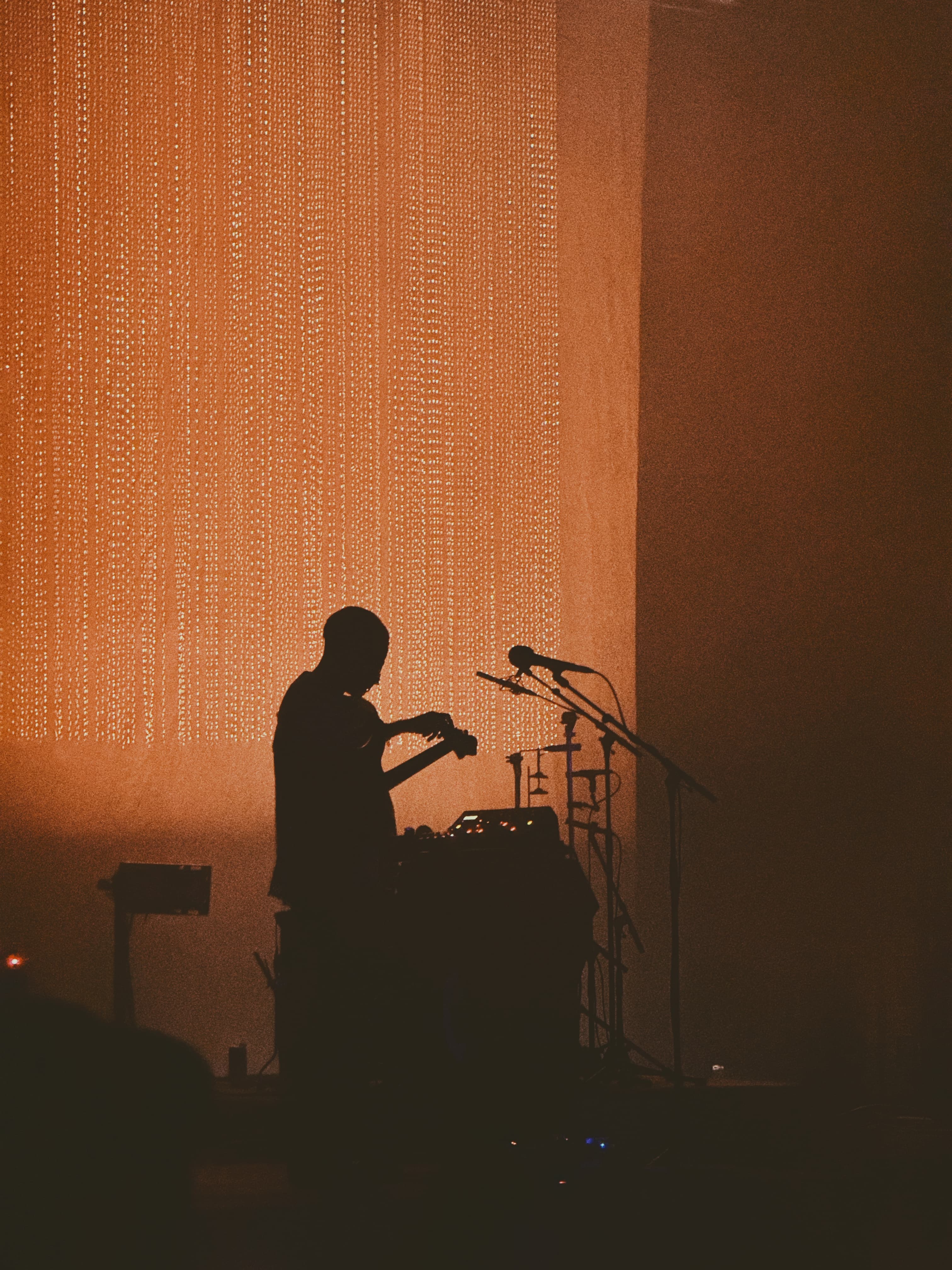 Glass Beams performer silhouetted against a curtain of warm orange lights
