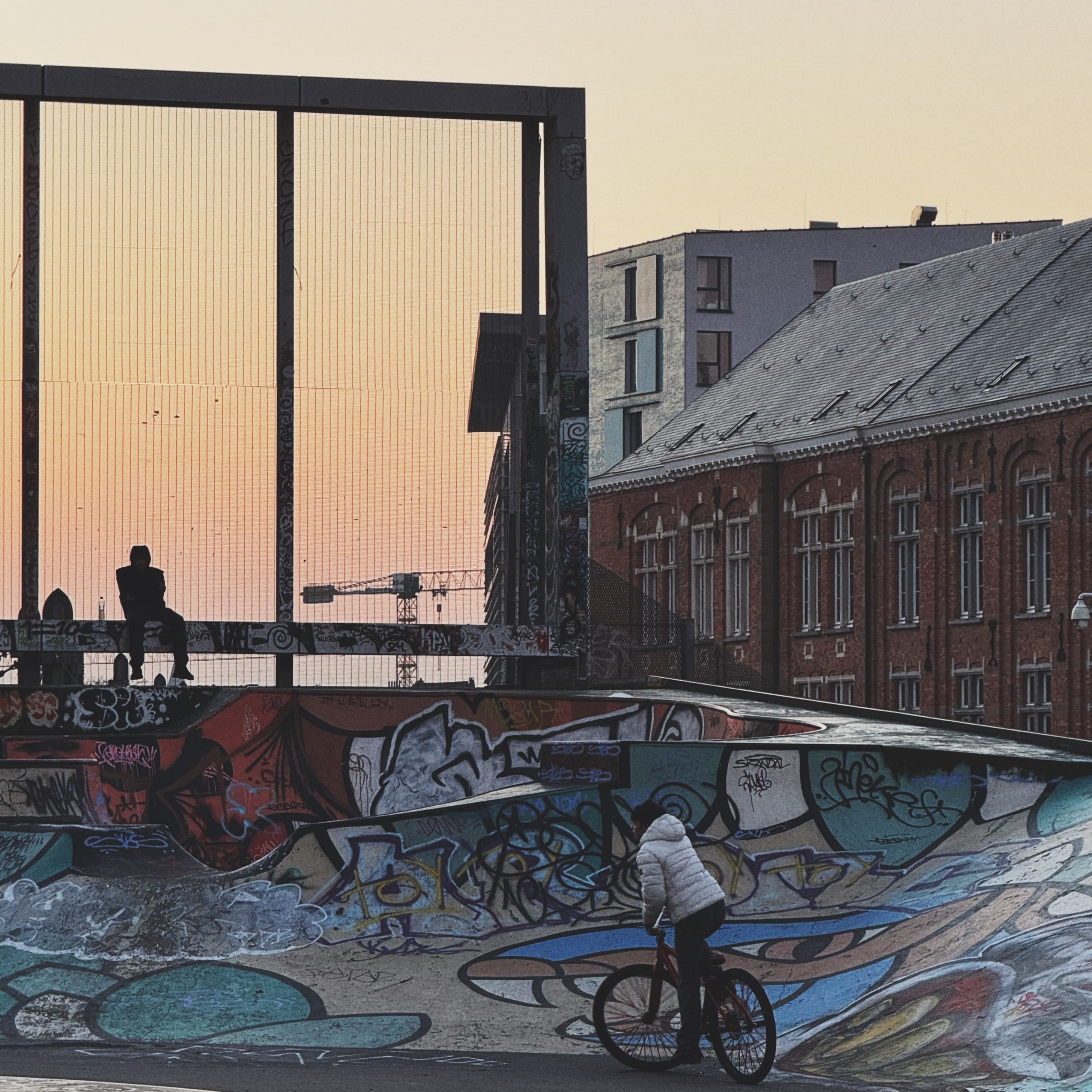 BMX rider in a graffiti-covered skate bowl beside a brick warehouse